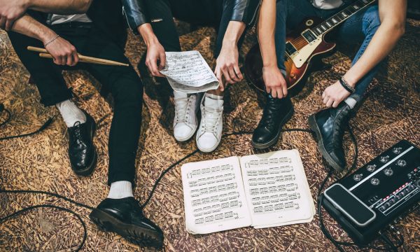 Repetition of rock music band. Cropped image of guitar players and drummer are sitting on the floor at rehearsal base with notes. Top view